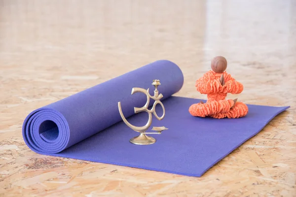 Figurine in orange clothes sitting in a yoga pose with a purple mat for exercise and meditation