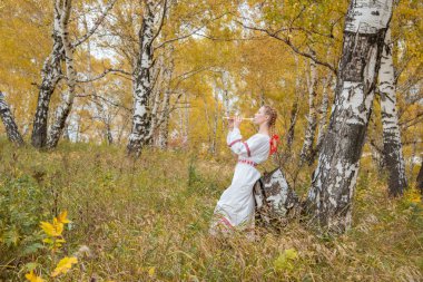Sonbahar ormanında flüt çalan Slav kıyafetleri içinde örgülü güzel kız