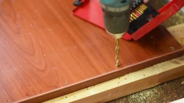 Bir adam mobilya monte etmek için tahtadan kahverengi bir tahtaya delikler açıyor.