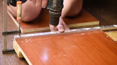 Bir adam mobilya monte etmek için tahtadan kahverengi bir tahtaya delikler açıyor.