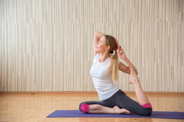 Hermosa chica rubia practica yoga asanas y se estira en una r — Foto de Stock