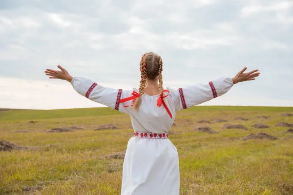 A girl in a Slavic dress with a red ribbon in her hair is standi — Stock Photo, Image