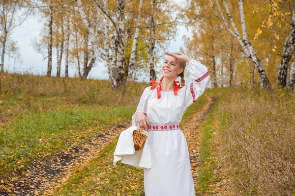Όμορφο κορίτσι σε ένα παραδοσιακό σλαβικό φόρεμα με ένα καλάθι άχυρο — Φωτογραφία Αρχείου