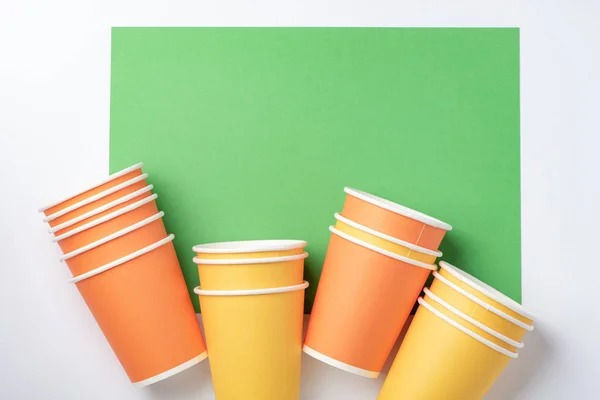 Tazas de papel naranja y amarillo sobre fondo blanco y verde — Foto de Stock