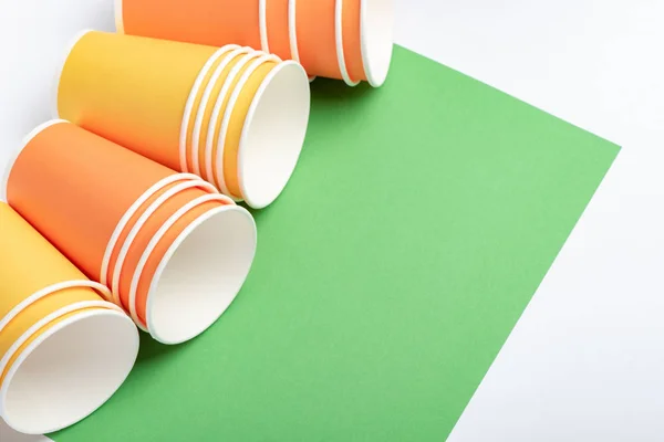 Tazas de papel naranja y amarillo sobre fondo blanco y verde — Foto de Stock
