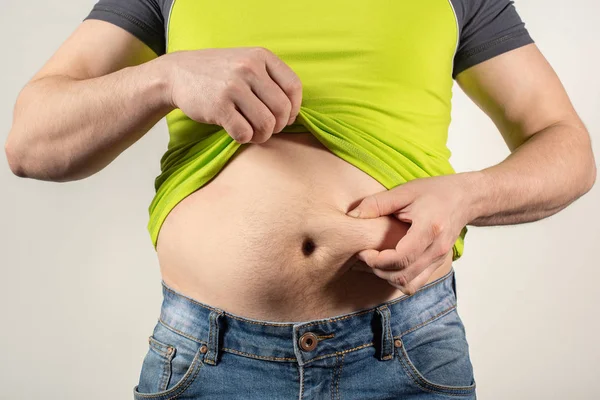 Un hombre en jeans y una camiseta con el vientre gordo sobre un fondo blanco — Foto de Stock