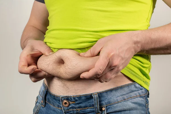 Un hombre en jeans y una camiseta con el vientre gordo sobre un fondo blanco — Foto de Stock