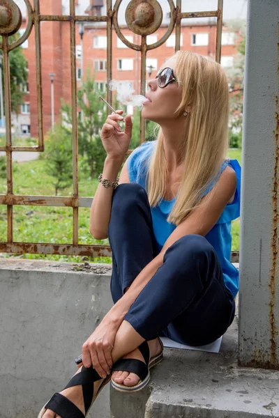 Mulher loira bonita fuma um cigarro branco enquanto agachamento n — Fotografia de Stock