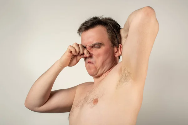 Um homem com axilas malcheirosas segura o nariz com a mão num espeto — Fotografia de Stock