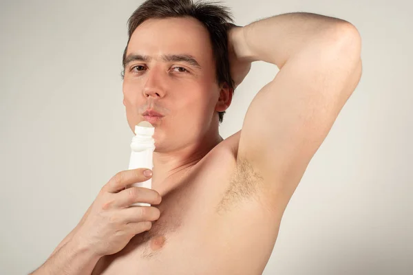 Handsome man with armpits holding a roll-on deodorant in his han