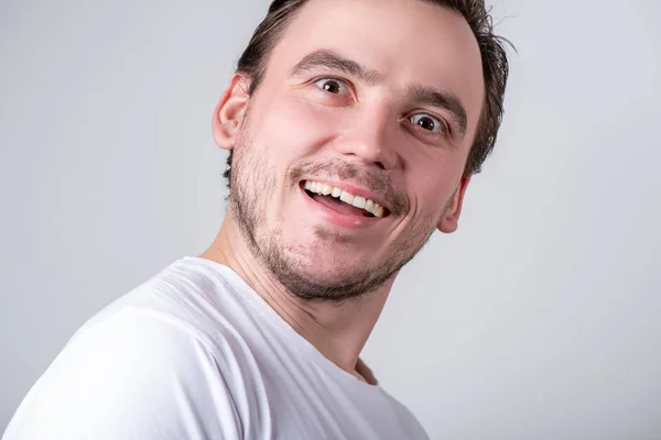 Handsome guy with bristles in a white T-shirt makes funny grimac — Stock Photo, Image