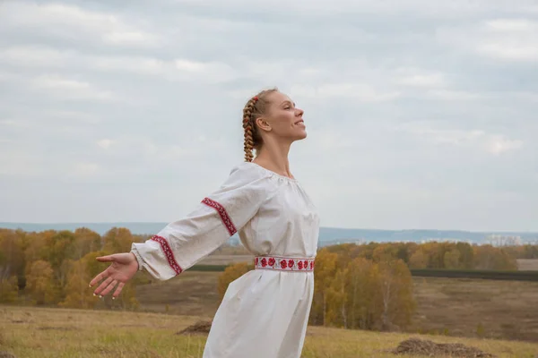 A girl in a Slavic dress with a red ribbon in her hair is standi — Stock Photo, Image