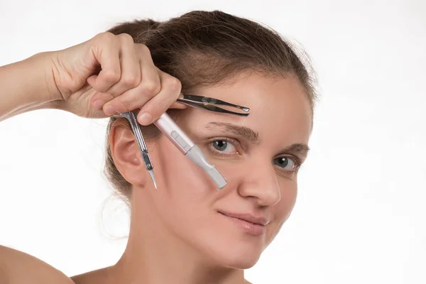 Young girl pulls out her eyebrows with tweezers metal on a white — Stock Photo, Image