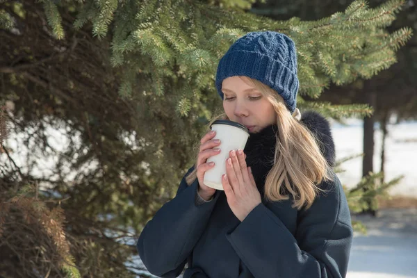 Beautiful girl walking in winter park and drink delicious hot co — Stock Photo, Image