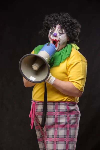 Scary clown shouting into a megaphone on a black background — Stock Photo, Image