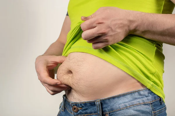 Un hombre en jeans y una camiseta con el vientre gordo sobre un fondo blanco — Foto de Stock