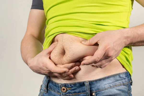 Un hombre en jeans y una camiseta con el vientre gordo sobre un fondo blanco — Foto de Stock