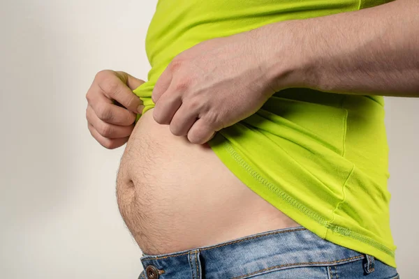 Un uomo in jeans e una t-shirt con la pancia grassa su uno schienale bianco — Foto Stock