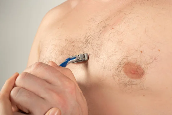 Zbliżenie męskiej klatki piersiowej z włosami i dłoni trzymanie maszynki do golenia na WHIT — Zdjęcie stockowe