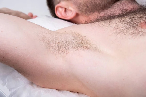 Closeup of male armpit with hair. A man is lying on a couch and