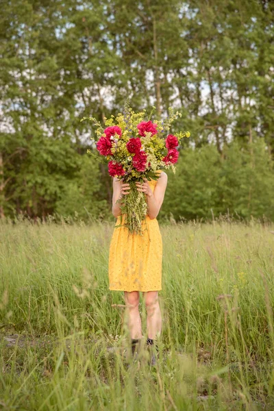 Uma menina em um vestido detém um grande buquê com peônias e selvagem fl — Fotografia de Stock