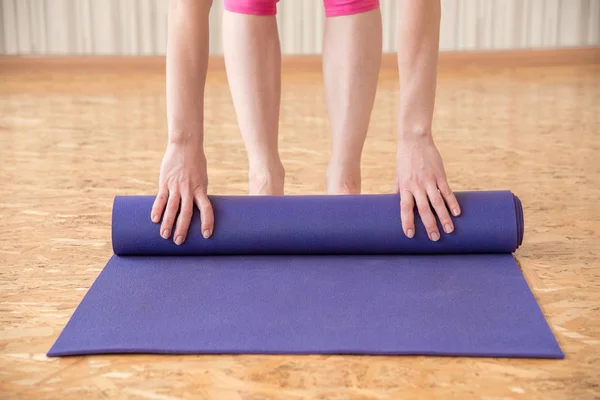 Mujer delgada despliega estera púrpura para gimnasia o yoga en el g — Foto de Stock