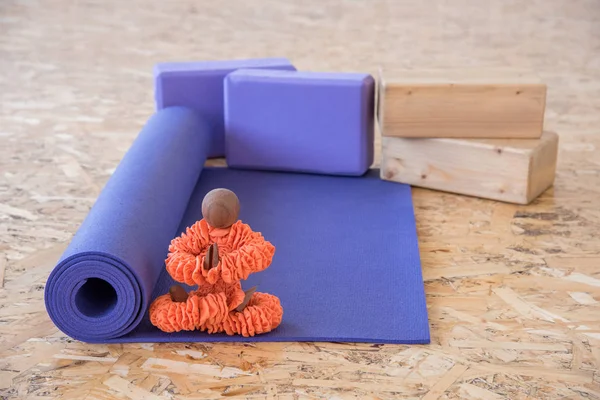 Figurine in orange clothes sitting in a yoga pose with a mat for