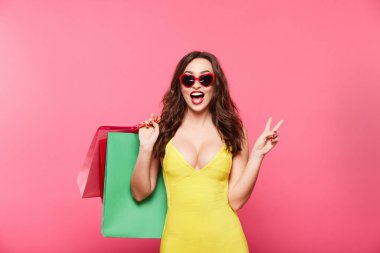 Genç kadın renkli alışveriş torbaları pembe arka plan, alışveriş ve indirim kavramı karşı tutan güneş gözlüğü takıyor