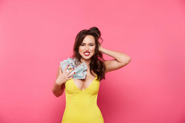 attractive alluring woman in yellow dress posing against pink background holding cash, shopping concept