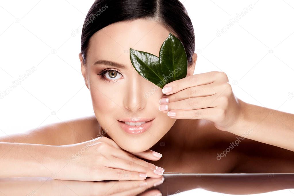 beautiful and natural young woman posing with green leaves isolated over white background, skin care concept, hydrated skin