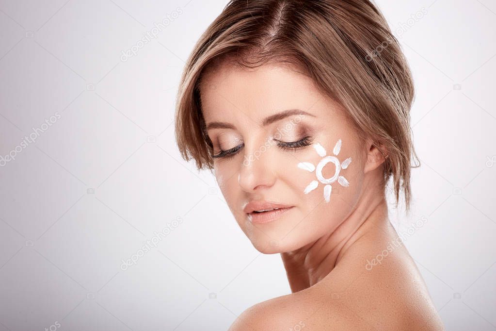 pretty smiling young woman using facial cream at grey background, beauty photo, skin care, spa concept
