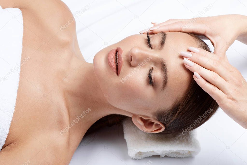 young woman with perfect skin having facial massage, hands on face, skin care, spa procedure and relaxing concept 