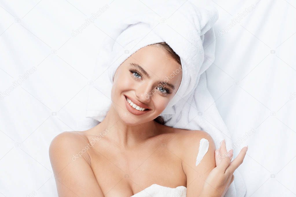 pretty smiling young woman using cream at white background, towel on head, beauty photo, skin care, spa concept