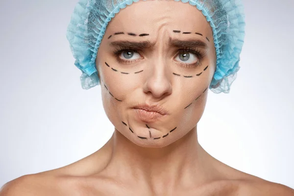beauty portrait of skeptical woman, plastic surgery concept. Model in blue cap with puncture lines on face