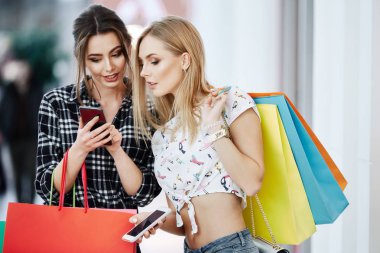 Alışveriş merkezinde cep telefonunu kullanarak renkli alışveriş torbaları ile genç ve güzel kadınlar