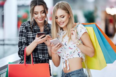 Alışveriş merkezinde cep telefonunu kullanarak renkli alışveriş torbaları ile genç ve güzel kadınlar