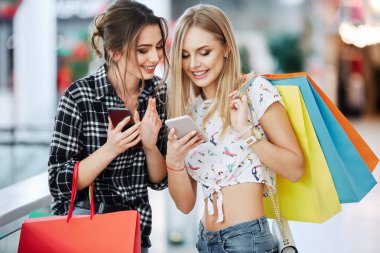 Alışveriş merkezinde cep telefonunu kullanarak renkli alışveriş torbaları ile genç ve güzel kadınlar
