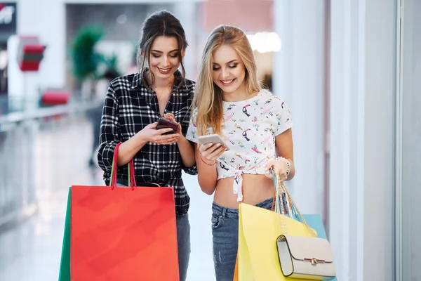 在购物中心使用移动电话的美丽的年轻妇女与五颜六色的购物袋 — 图库照片