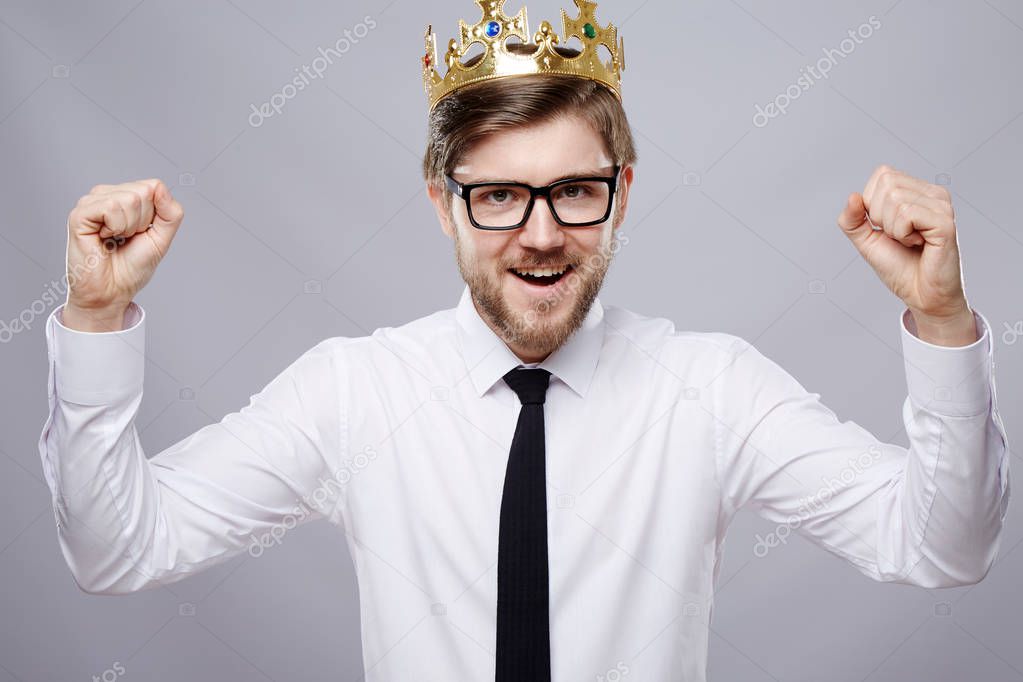 happy attractive man wearing white shirt, tie, crown and glasses over grey background, business concept