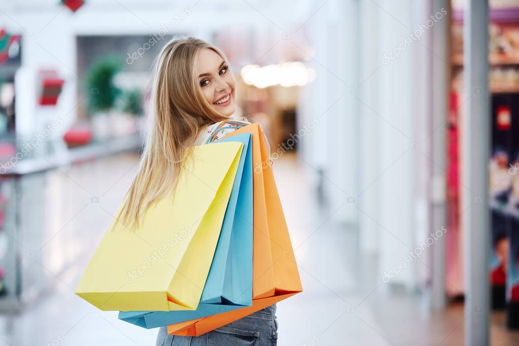 beautiful blonde young woman posing with colorful shopping bags at shopping mall