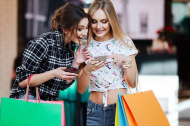Alışveriş merkezinde cep telefonunu kullanarak renkli alışveriş torbaları ile genç ve güzel kadınlar