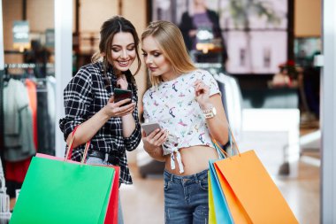 Alışveriş merkezinde cep telefonunu kullanarak renkli alışveriş torbaları ile genç ve güzel kadınlar