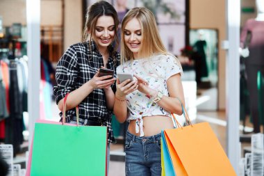 Alışveriş merkezinde cep telefonunu kullanarak renkli alışveriş torbaları ile genç ve güzel kadınlar