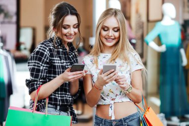 Alışveriş merkezinde cep telefonunu kullanarak renkli alışveriş torbaları ile genç ve güzel kadınlar
