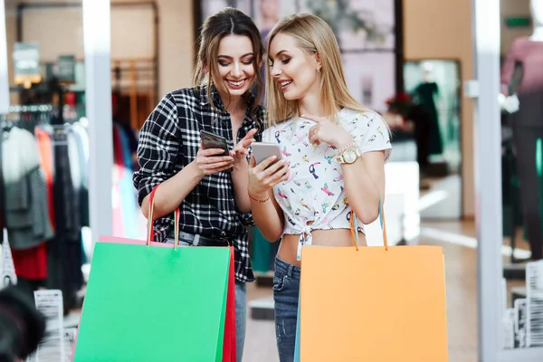 Alışveriş merkezinde cep telefonunu kullanarak renkli alışveriş torbaları ile genç ve güzel kadınlar
