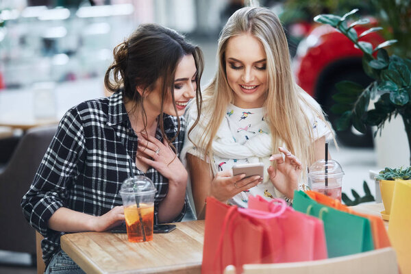 attractive young women using smartphones, colorful shopping bags on the table  in cafe