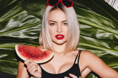 Sarışın genç kadın güneş gözlüğü ve kırmızı dudaklar karpuz dilimi Palm'da poz ile arka plan, seksi model bırakır