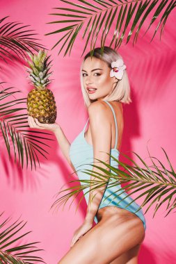 Genç kız mavi sarı saçlı giyen ile mayo pembe arka plan poz ananas holding
