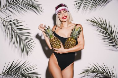 Sarı saçlı giyen ile güzel kız siyah takım elbise ve ananas ile pembe kap ayakta beyaz stüdyo arka plan avuç içi, seksi modeli ile yüzme
