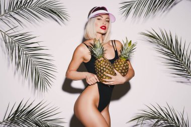 Sarı saçlı giyen ile güzel kız siyah takım elbise ve ananas ile pembe kap ayakta beyaz stüdyo arka plan avuç içi, seksi modeli ile yüzme